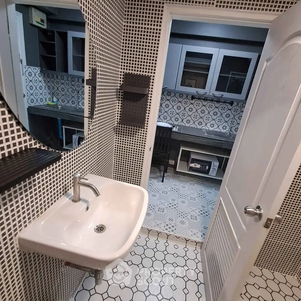 Stylish bathroom with modern sink and patterned tiles leading to a chic study area.