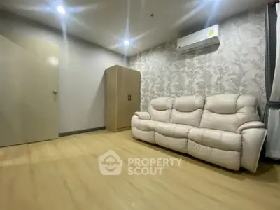 Spacious living room with modern sofa and air conditioning, featuring elegant wallpaper and wooden flooring.