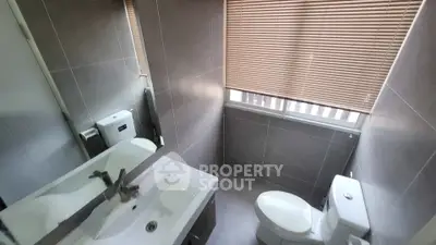 Modern bathroom with sleek fixtures and natural light from window blinds.