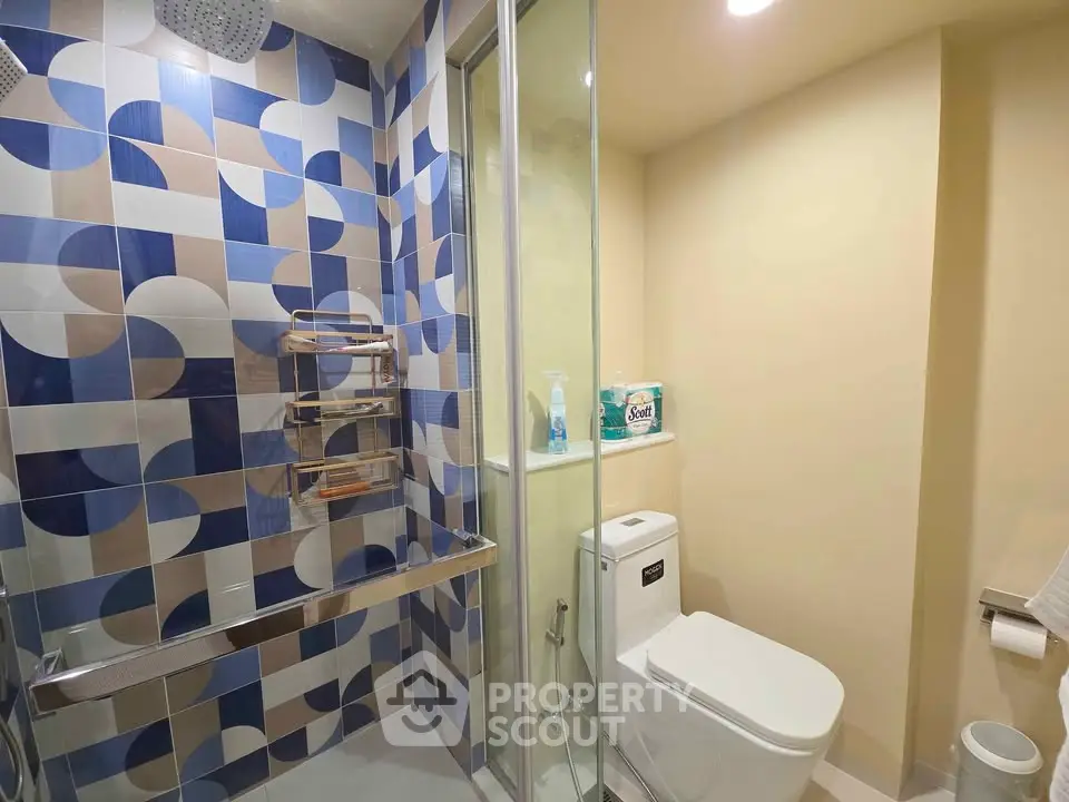 Modern bathroom with geometric tile design and glass shower enclosure.