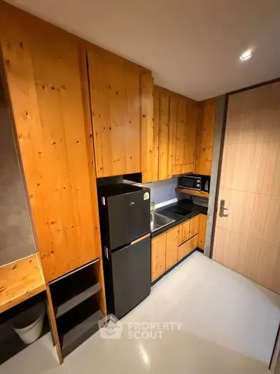 Modern compact kitchen with wooden cabinets and sleek appliances in a cozy apartment.