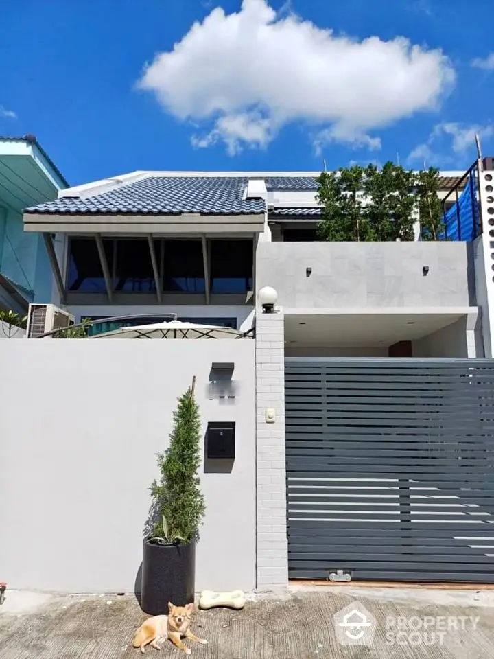 Modern two-story house with sleek design and gated entrance under a clear blue sky.