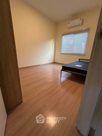 Spacious and well-lit bedroom with polished wooden flooring and a large window, perfect for comfortable living.