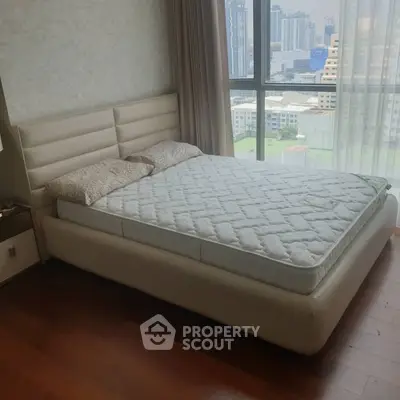 Spacious bedroom with city view, featuring a modern bed and large windows for natural light.