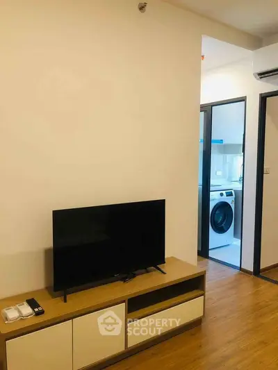 Modern living room with TV and view into laundry area with washing machine.