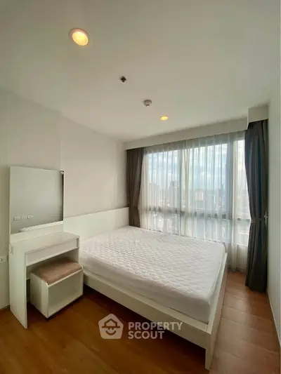 Bright and airy bedroom with large window and modern furnishings in a high-rise apartment.