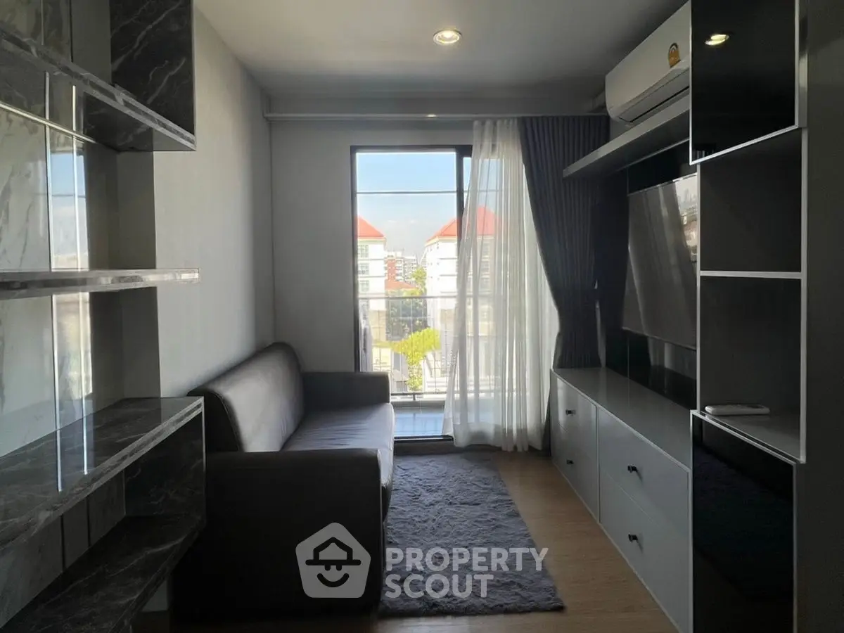 Modern living room with sleek furniture and large window offering city view.