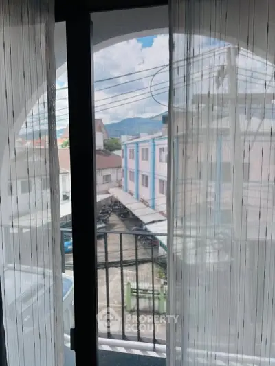 Charming balcony view with sheer curtains overlooking urban neighborhood and distant mountains.