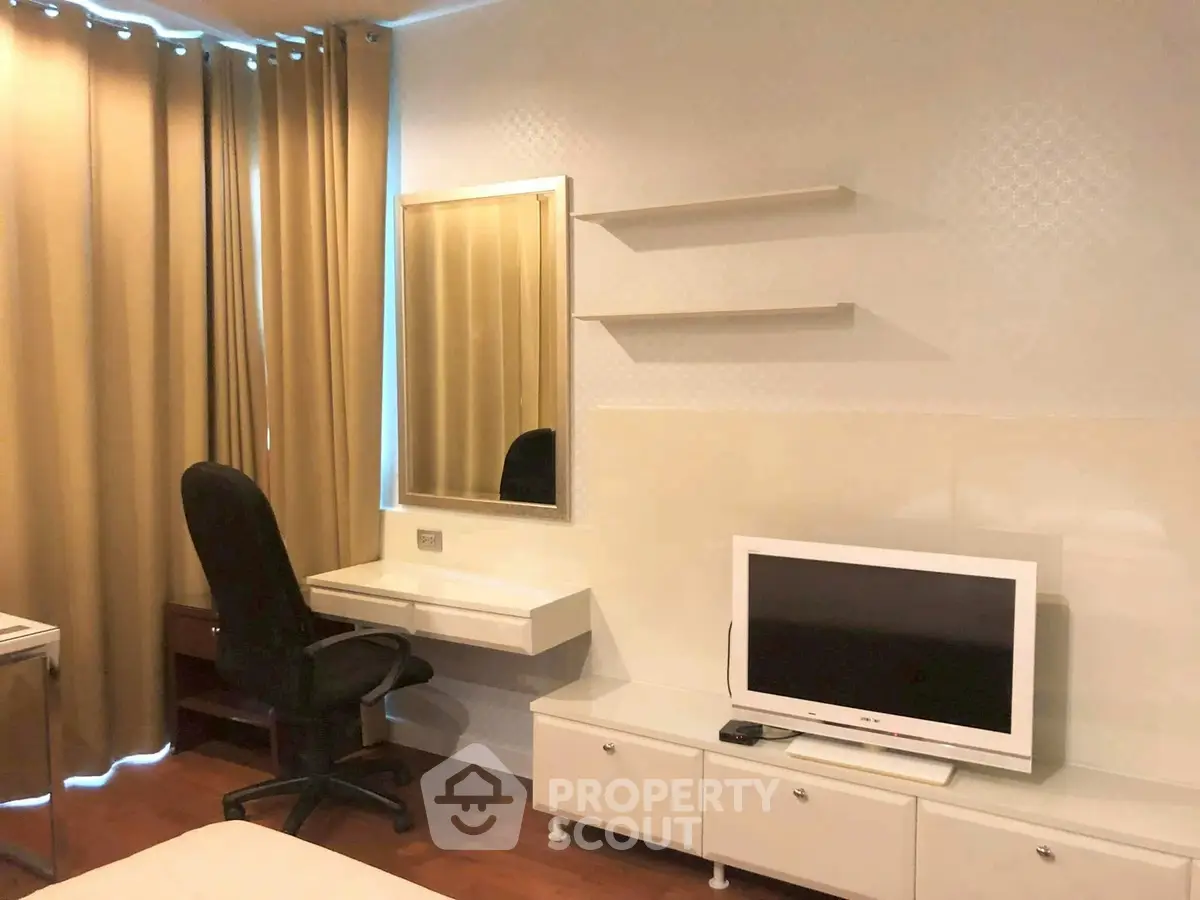 Modern bedroom with TV, desk, and mirror, featuring elegant curtains and wooden flooring.