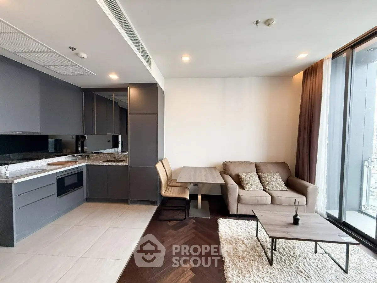 Modern open-layout living room with sleek kitchen and cozy seating area, featuring large windows and stylish decor.