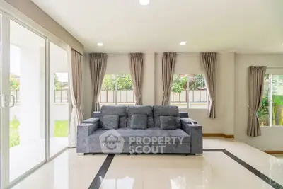 Spacious living room with modern gray sofa and large windows overlooking garden.