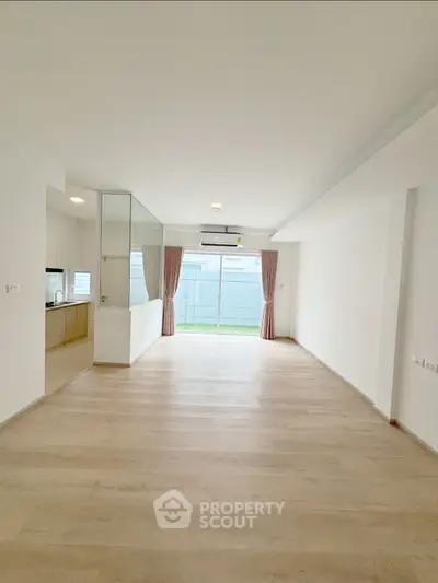 Spacious open-plan living room with wooden flooring and large windows for natural light.