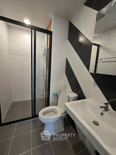 Modern bathroom with sleek black and white tiles, glass shower enclosure, and contemporary fixtures.
