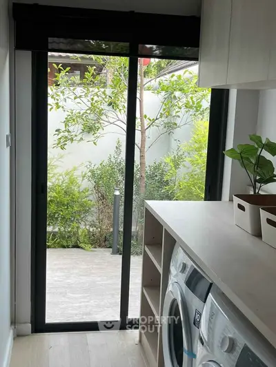 Modern laundry room with washing machine and sliding glass door leading to a lush garden view.
