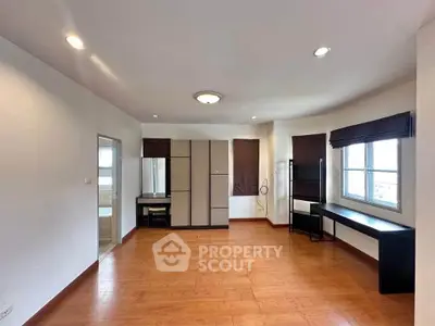 Spacious unfurnished room with wooden flooring and large windows in modern apartment.