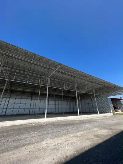 Spacious industrial warehouse with high ceilings and open layout under clear blue sky.