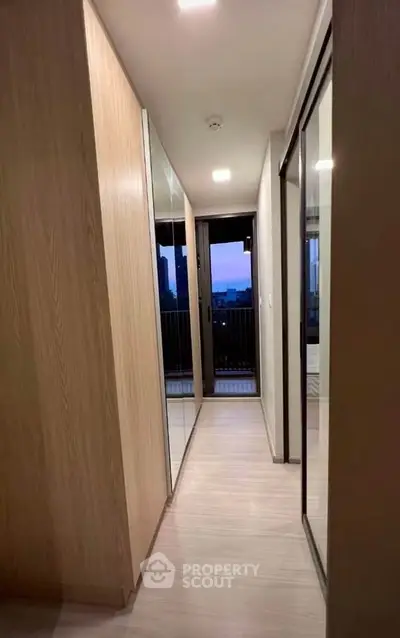 Modern hallway with mirrored closets leading to a balcony with city view.
