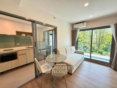 Modern living room with open kitchen and balcony view, featuring sleek furniture and natural light.