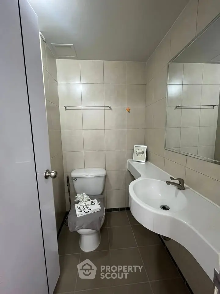 Modern bathroom with sleek fixtures and neutral tiles, featuring a stylish curved sink and wall-mounted mirror.