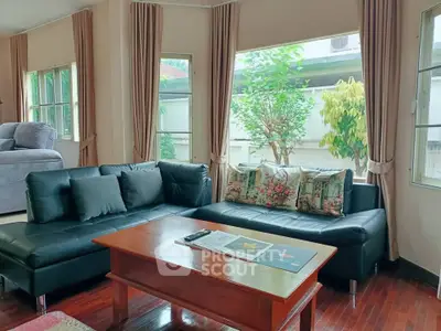Spacious living room with elegant black sofas and large windows offering garden views.