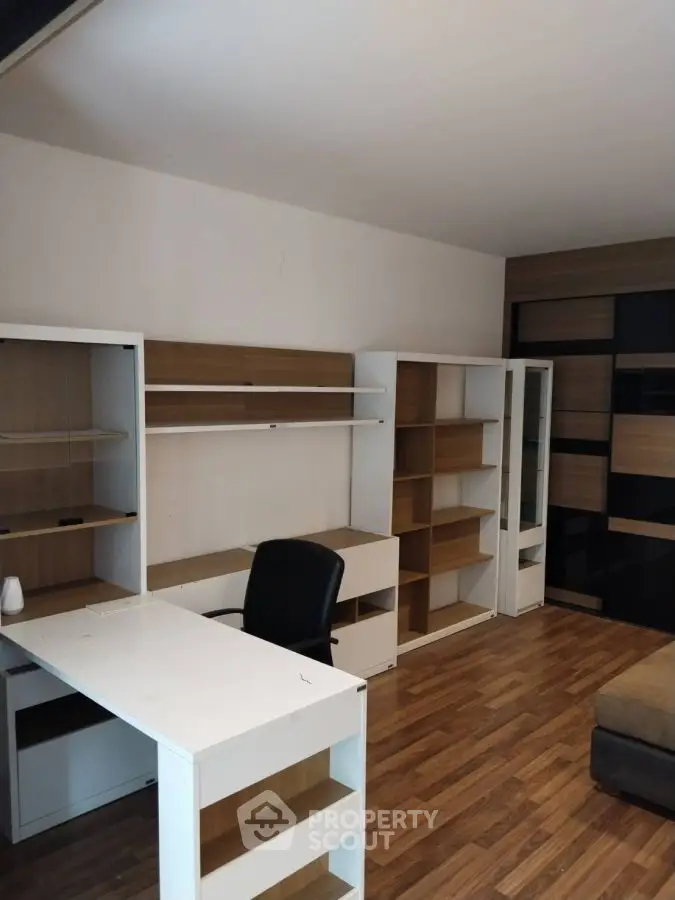 Modern study room with sleek white desk and ample shelving on wooden flooring.