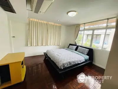 Spacious bedroom with polished hardwood floors, large windows allowing natural light, and modern furnishings for a comfortable living experience.