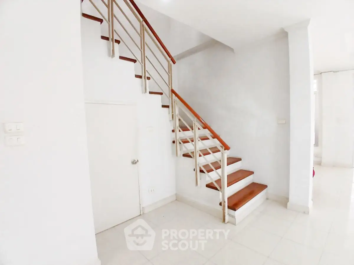 Modern staircase with wooden steps and sleek railing in a bright interior space.