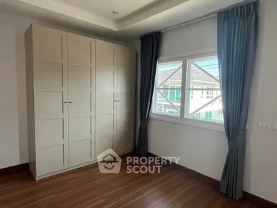 Spacious bedroom with large window and stylish wardrobe, offering natural light and modern design.