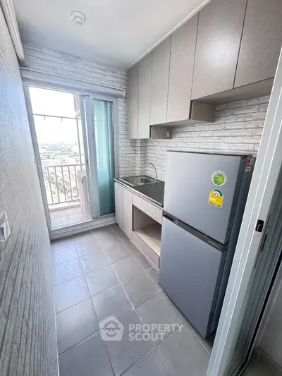 Modern kitchen with balcony view, featuring sleek cabinets and stainless steel fridge.