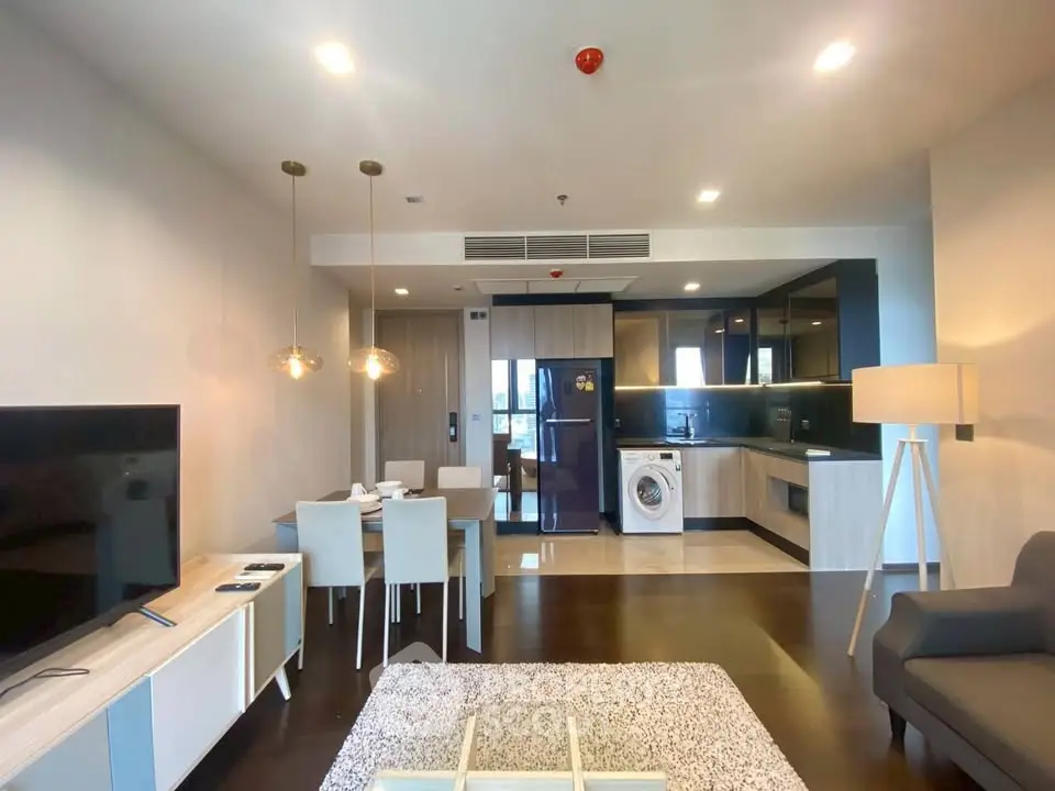 Modern open-plan living room with kitchen and dining area, featuring sleek furniture and appliances.