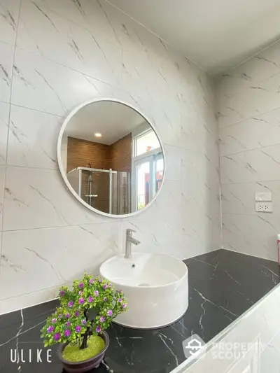 Elegant bathroom with marble walls, modern round sink, and stylish mirror reflecting a well-lit interior space, ideal for contemporary living.