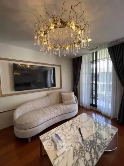 Luxurious living room with elegant chandelier and marble coffee table, featuring a plush sofa and large TV.