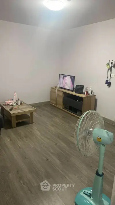 Cozy living room with modern decor and wooden flooring, featuring a TV and fan for comfort.