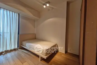 Cozy bedroom with wooden flooring and natural light through sheer curtains.