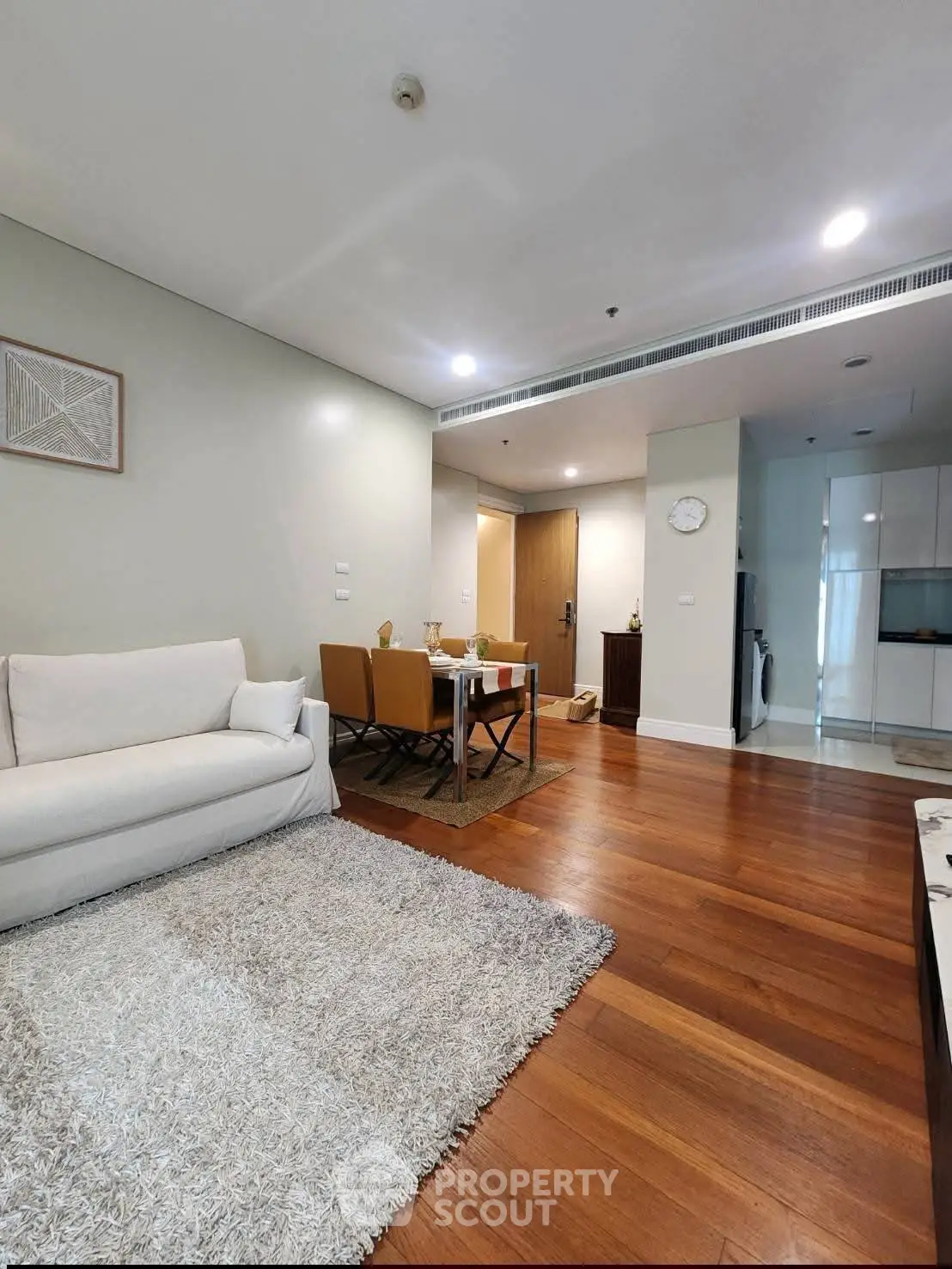 Modern living room with hardwood floors, cozy rug, and elegant dining area in open layout apartment.
