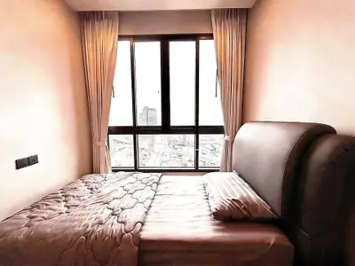 Cozy bedroom with large window offering city view, featuring elegant curtains and plush bedding.