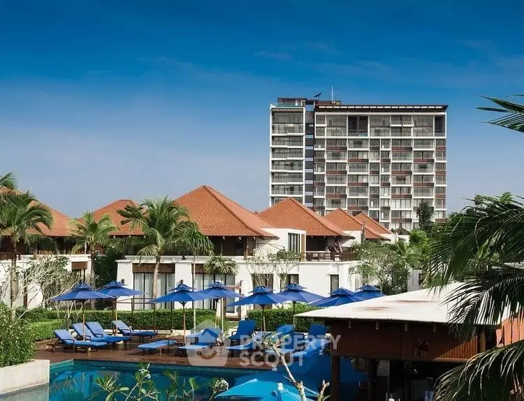 Luxurious resort with poolside view and modern high-rise building under clear blue sky.