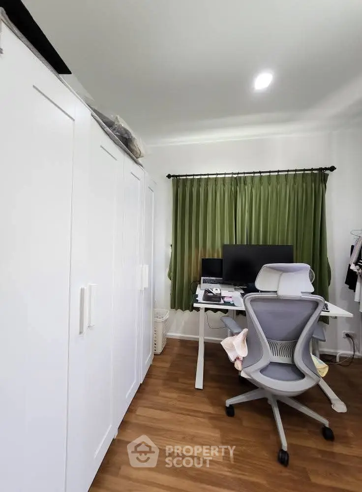 Modern study room with ergonomic chair and large desk, featuring green curtains and ample storage space.