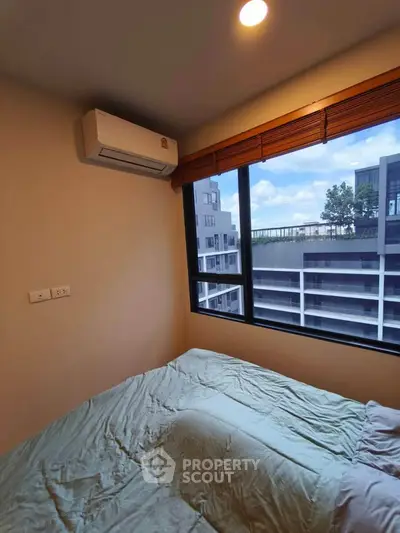 Cozy bedroom with large window offering city view and air conditioning unit.