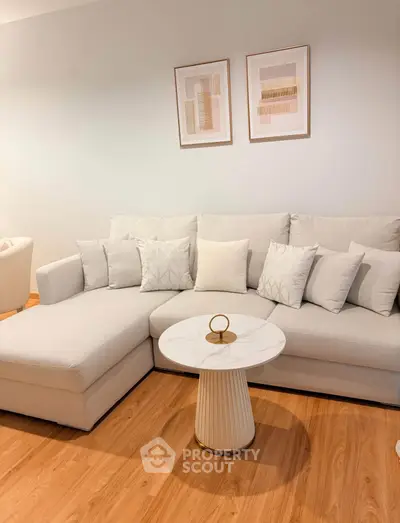 Elegant living room with modern white sectional sofa and stylish round coffee table on wooden flooring.