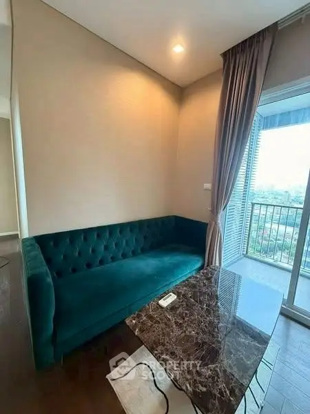 Elegant living room with plush green sofa and marble coffee table, featuring a balcony with city view.