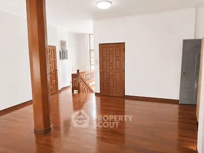 Spacious wooden-floored room with elegant staircase and natural light