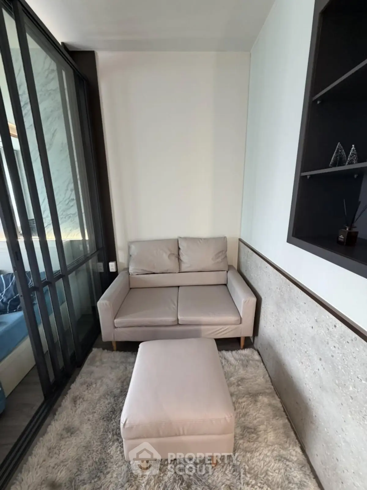 Cozy small living area with modern sofa and ottoman on plush rug, adjacent to glass partition.