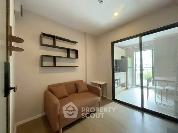 Modern living room with cozy sofa and open kitchen layout, featuring sleek shelving and bright natural light.