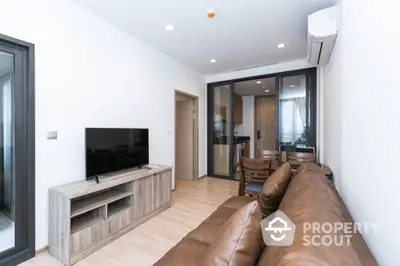 Modern living room with leather sofa and TV, open layout to kitchen area