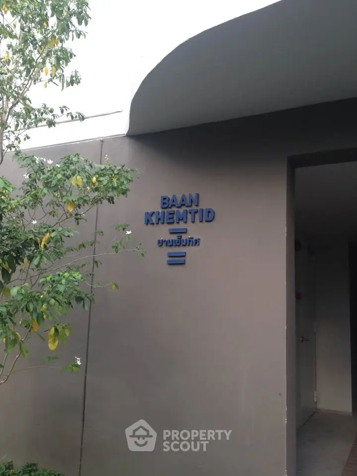 Modern building entrance with sleek design and greenery, showcasing Baan Khemtid signage.