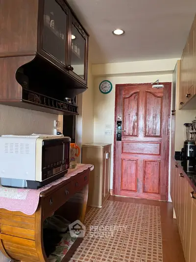 Charming kitchen with wooden cabinets and modern appliances, featuring a warm wooden door and tiled floor.