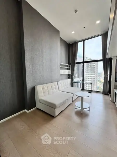 Modern living room with high ceilings and large windows offering city views.
