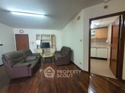 Spacious living room with leather sofas and wooden flooring adjacent to a modern kitchen.