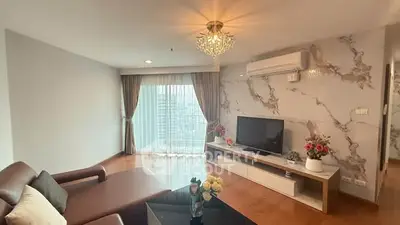 Spacious living room with elegant decor and city view, featuring a modern chandelier and stylish furnishings.